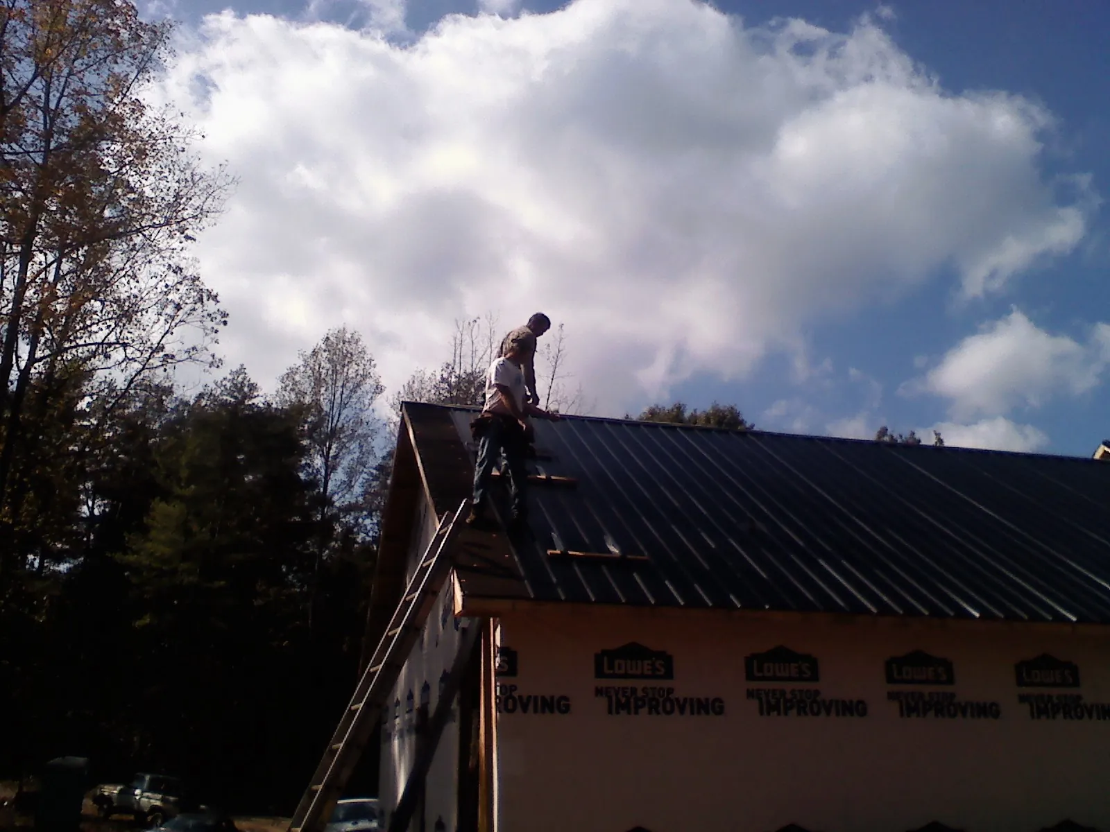 Roofer fastening dark metal panels high against a cloudy sky, from a Roof Inspection job in Townsville